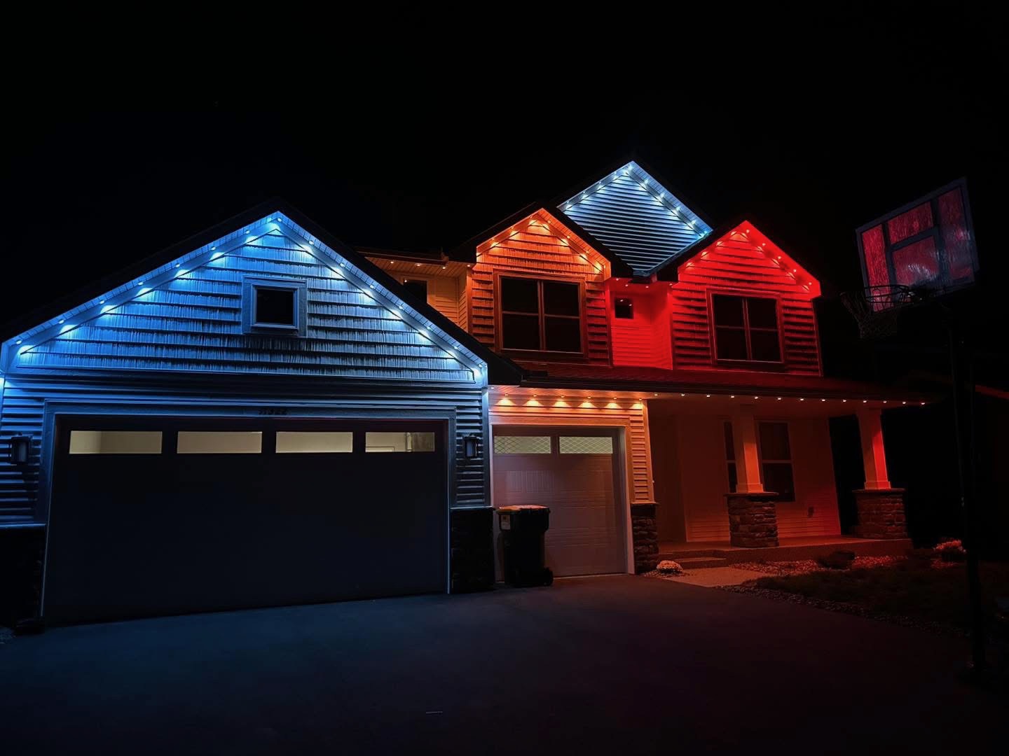 Two-story home lit with blue, white and red permanent LED roofline lighting at night