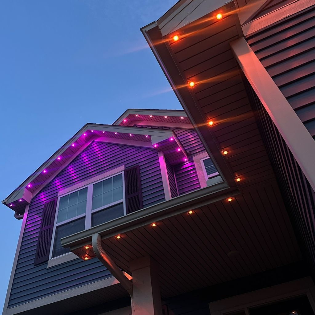Close-up of permanent LED lights glowing purple and warm amber along a roofline at dusk